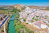 Aerial view of the white houses that go all the way to the top of the cliff and the turquoise river along the side of the town of Arcos de la Frontera, Andalusia, Spain.