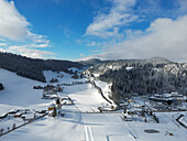 Luftaufnahme einer verschneiten Landschaft mit Bergen, Bäumen und Feldern, Col-des-Roches, Schweiz.