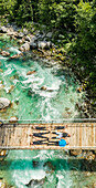Aerial view of sporty family lying on wooden suspension bridge above a river.