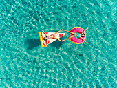 Aerial view of two young girls floating in sea on pizza and donut shaped inflatables touching feet.