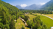 Aerial view of a campsite in the middle of pine forest with mountains in the background in Soca valley, Bovec, Slovenia.
