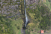 Aerial view of cascata do poco do bacalhau waterfall cascading down a lush green cliff surrounded by serene forest, Faja Grande, Portugal.