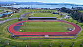 Aerial view of a scenic sports field and track surrounded by greenery and mountains with a lake, Nelson, New Zealand.