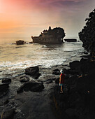 Aerial view of a person enjoying the view of Tanah Lot Temple at sunset in Bali, Indonesia.