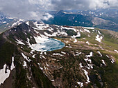 Aerial view of majestic snowy mountains and a serene lake surrounded by clouds, Sambaksar Pass, Gilgit Baltistan, Pakistan.