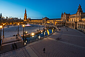 As twilight descends on Seville, lights reflect on the water at Plaza de Espana, creating a tranquil atmosphere for evening strolls.