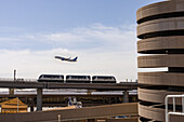 A Sky Train passenger transit train with an airliner taking off at Phoenix Sky Harbor Airport, Arizona. At right is the spiral ramp for the parking garage building.