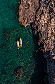 Luftaufnahme eines Paares, das sich auf Paddelbrettern in den klaren Gewässern von Polignano a Mare, Apulien, Italien, entspannt