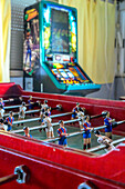 Groups of friends play spirited foosball at a village bar in Puebla del Maestre, enjoying drinks and camaraderie under bright lights.