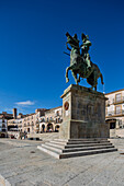 Visitors admire Pizarro's statue in the vibrant Plaza Mayor of Trujillo, surrounded by historical buildings and clear blue skies.