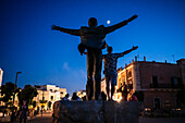 Silhouette for a man posing for a photo emulating the Statue of Domenico Modugno in Polignano a Mare at night with the moon in the background, Puglia, Italy