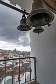 Kirchenglocken in einem Glockenturm der Kirche San Francisco in Quito, Ecuador, mit der Basilica del Voto Nacional im Hintergrund.