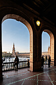 Visitors gather on a balcony at Plaza de Espana in Seville, enjoying late afternoon light and stunning architecture framed by arches.