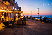 People enjoying dinner at sunset in a restaurant terrace in Polignano a Mare, Puglia, Italy