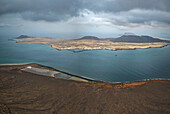 Panoramic view of La Graciosa island from the Famara cliffs in Lanzarote, showing the Salinas del Río (in Lanzarote), the village of Caleta del Sebo on La Graciosa, and the islands of Montaña Blanca and Alegranza in the background.
