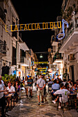 Via Roma, a street lined with restaurants and decorated with hanging lights with phrases from Domenico Modugno's songs, Polignano a Mare, Italy