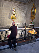 A man kneeling & worshipping at a side chapel in the Basilica del Voto Nacional in Quito, Ecuador.