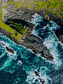 Luftaufnahme von zerklüfteten Klippen und krachenden Wellen mit einer malerischen Küstenlinie, Foilnageragh, Kerry, Irland.