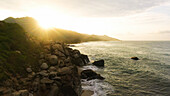 Aerial view of a beautiful sunrise over the tropical beach with waves crashing on rugged rocks, Santa Marta, Magdalena, Colombia.
