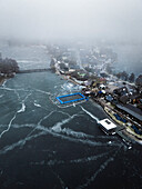 Aerial view of a serene winter landscape with a frozen lake, village, and bridge, Trakai, Trakai, Lithuania.
