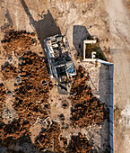 Aerial view of a construction site with exposed earth, heavy machinery, and a partly built structure, contrasting with the surrounding fence, Sa'ar, North District, Israel.