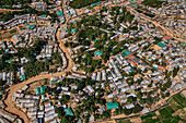 Aerial view of tightly packed dwellings interspersed with green trees and winding pathways creating a textured landscape, Balukhali Bazar, Chittagong Division, Bangladesh.