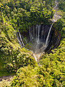 Aerial view of the cascading Tumpak Sewu Waterfall plunges into a verdant amphitheater, a stunning contrast to the surrounding lush jungle, Gunungsriti, Jawa Timur, Indonesia.