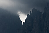 Blick auf zerklüftete, dunkle Berggipfel, die durch einen Schleier aus wirbelndem Nebel und bedrohlichen Wolken stechen, St. Ulrich, Trentino-Südtirol, Italien.