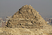 Blick auf die antike Pyramide, deren verwitterte Steine in der Sonne glühen, vor dem Hintergrund einer dunstigen Skyline, eine Reise durch die Zeit, Kairo, Ägypten.
