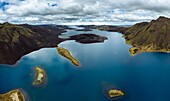Aerial view of deep blue waters reflecting the cloudy sky and surrounding rugged, dark mountains with patches of green, Iceland.