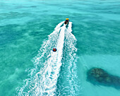 Aerial view of people enjoying a funtube behind a boat over turquoise water and vibrant corals, Vashafaru, Haa Alif, Maldives.