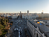 Aerial view of the bustling Plaza Cibeles with historic buildings and vibrant flags, Centro, Madrid, Spain.