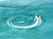 Aerial view of people on a funtube being towed by a boat over beautiful turquoise corals in the clear ocean, Vashafaru, Haa Alif, Maldives.