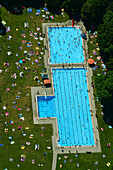 Aerial view of crowded public pool with people swimming and sunbathing surrounded by grass and trees, Schwabing-West, Bayern, Germany.