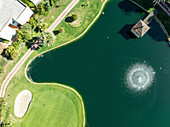Luftaufnahme des La Noria Golf Resorts mit einem ruhigen See, einem stillen Springbrunnen und einem üppig grünen Golfplatz, Calahonda-Chaparral, Mijas, Malaga, Spanien.