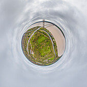 Aerial view of tiny planet perspective of Humber Bridge over the river surrounded by greenery under a cloudy sky, Hessle, England, United Kingdom.