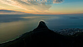Luftaufnahme der Silhouette des Löwenkopfs gegen die Wolken und den Ozean bei Sonnenuntergang, Kapstadt, Westkap, Südafrika.