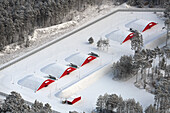 Aerial view of snowy bunker surrounded by tranquil forest and red buildings, Biesenthal, Brandenburg, Germany.