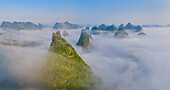 Luftaufnahme einer Aussichtsterrasse auf dem Berggipfel mit Blick auf die Berglandschaft von Guilin bei Sonnenaufgang mit tief hängenden Wolken, Guangxi, China.