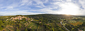 Luftaufnahme eines auf einem Hügel gelegenen Dorfes im goldenen Licht der untergehenden Sonne, umgeben von üppig grünen Bäumen und Feldern, Moissac-Bellevue, Provence-Alpes-C?te d'Azur, Frankreich.