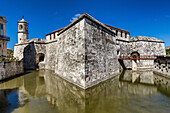View of a formidable stone fortress reflecting in a still moat under a vibrant blue sky, a testament to history and strength, Havana, Havana, Cuba.