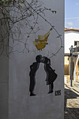 Lefkosia, Cyprus - 25 June 2025: View of a white wall adorned with a mural depicting children kissing beneath a yellow Cyprus map, framed by delicate, winding branches.