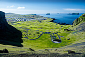 View of lush green valley meets the dark blue sea, framed by rugged cliffs in a striking contrast of nature's beauty, Vestmannaeyjabær, Vestmannaeyjabær, Iceland.