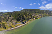 Aerial view of a serene lake mirroring the clear sky, embraced by lush green hills and a quaint structure nestled along the shore, Furnas, Azores, Portugal.