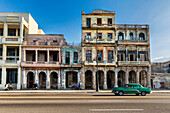 Havana, Cuba - 07 July 2025: View of aged, pastel-hued buildings stand proudly against the clear sky, while a vintage green car cruises along the sun-drenched street.