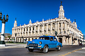 Havana, Cuba - 07 July 2025: View of a classic blue car gleaming against the ornate facade of the Gran Teatro de La Habana under a vibrant blue sky.