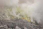 Blick auf ätherische Schwefelwolken, die aus der Vulkanlandschaft aufsteigen, eine Szene mit geothermischer Aktivität und felsigen Strukturen, Vulkankrater Ijen, Ost-Java, Indonesien.