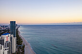 Luftaufnahme der Küstenlinie, Hochhäuser und der Atlantische Ozean treffen unter dem pastellfarbenen Himmel aufeinander und bilden eine ruhige städtische Meereslandschaft, Sunny Isles Beach, Florida, Vereinigte Staaten.