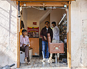 Bikaner, India - 24 June 2025: View of a local barbershop bathed in the warm sunlight, where three men gather amidst vintage furnishings and faded walls.