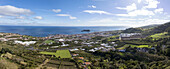 Luftaufnahme eines farbenfrohen Wandteppichs aus üppigen grünen Feldern und malerischen Häusern trifft auf den tiefblauen Ozean nahe der Insel Vila Franca do Campo, Vila Franca do Campo, Azoren, Portugal.